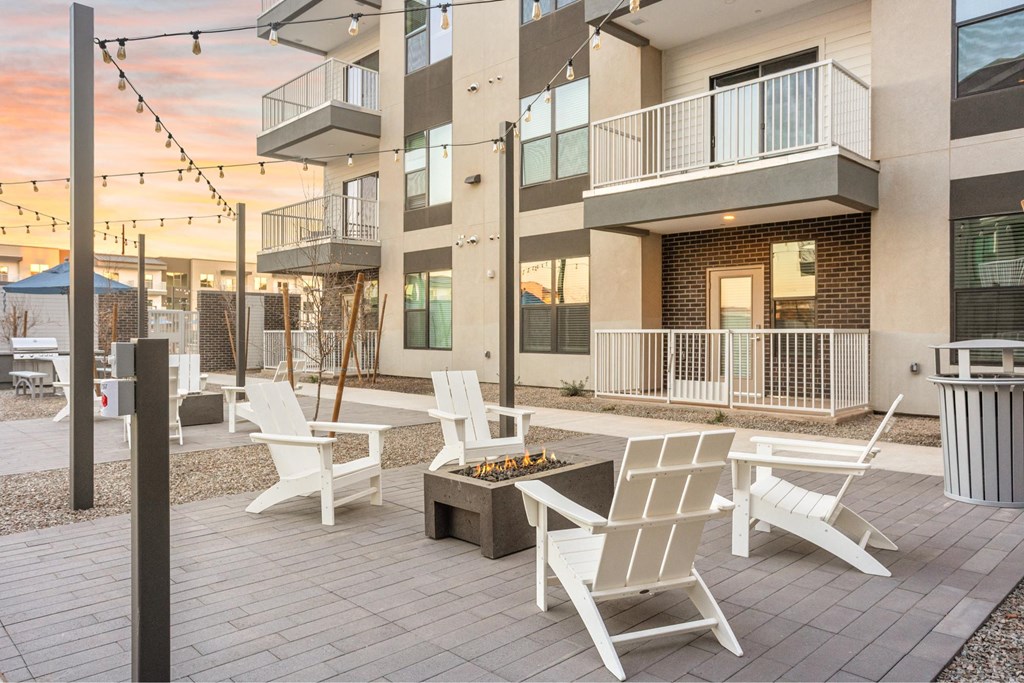 A patio with white chairs and a table is in front of a building.