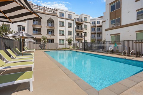 A swimming pool surrounded by sun loungers and apartment buildings.