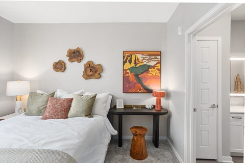 A bedroom with a bed, a table with a lamp, and a painting on the wall.