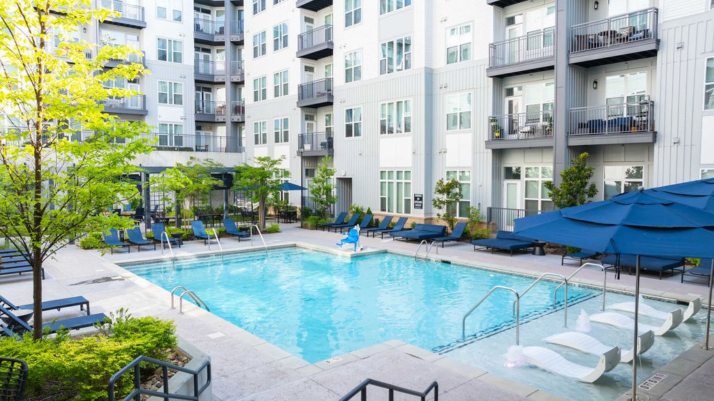 A swimming pool surrounded by lounge chairs and umbrellas in front of apartment buildings.