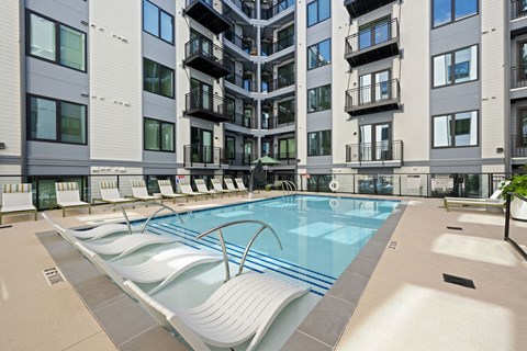 A large outdoor swimming pool with lounge chairs is surrounded by apartment buildings.