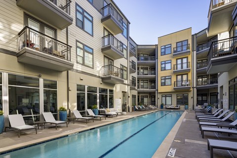 a swimming pool with chaise lounge chairs in front of an apartment building