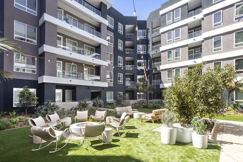 A large grassy area with chairs and plants in front of apartment buildings.