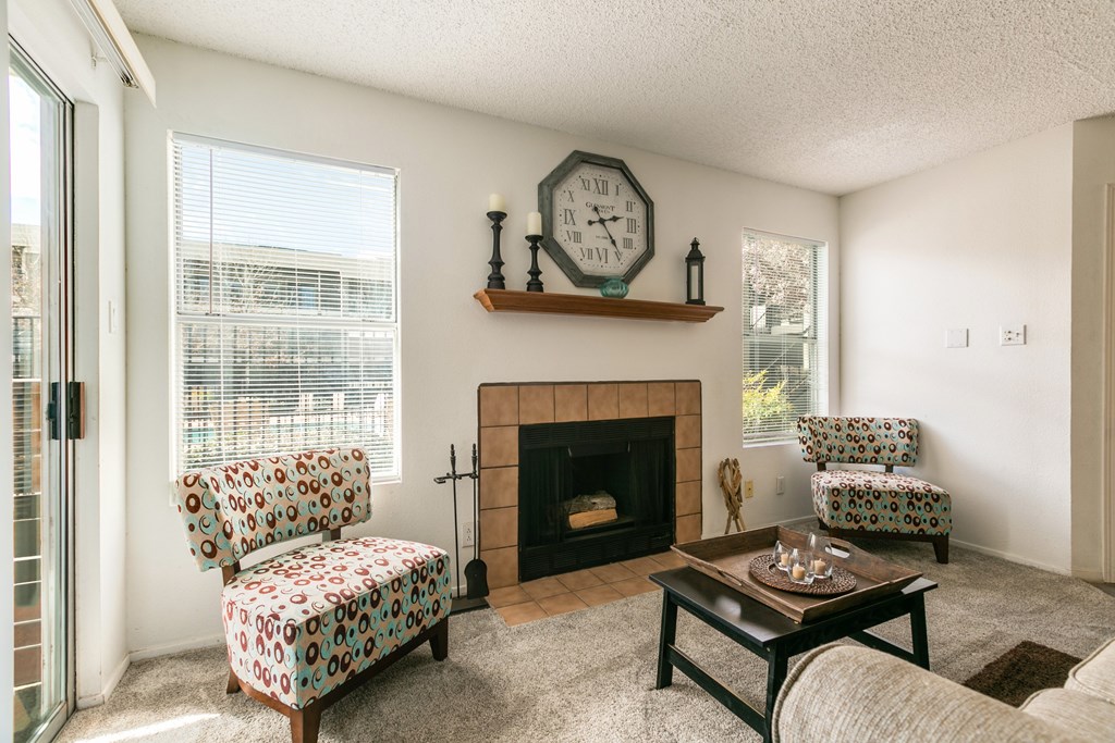 A living room with a fireplace, two chairs, and a clock on the wall.