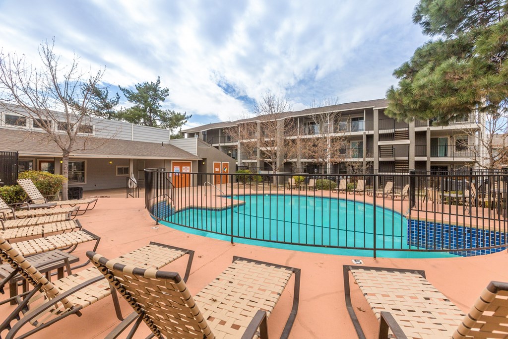A pool surrounded by chairs and a fence.