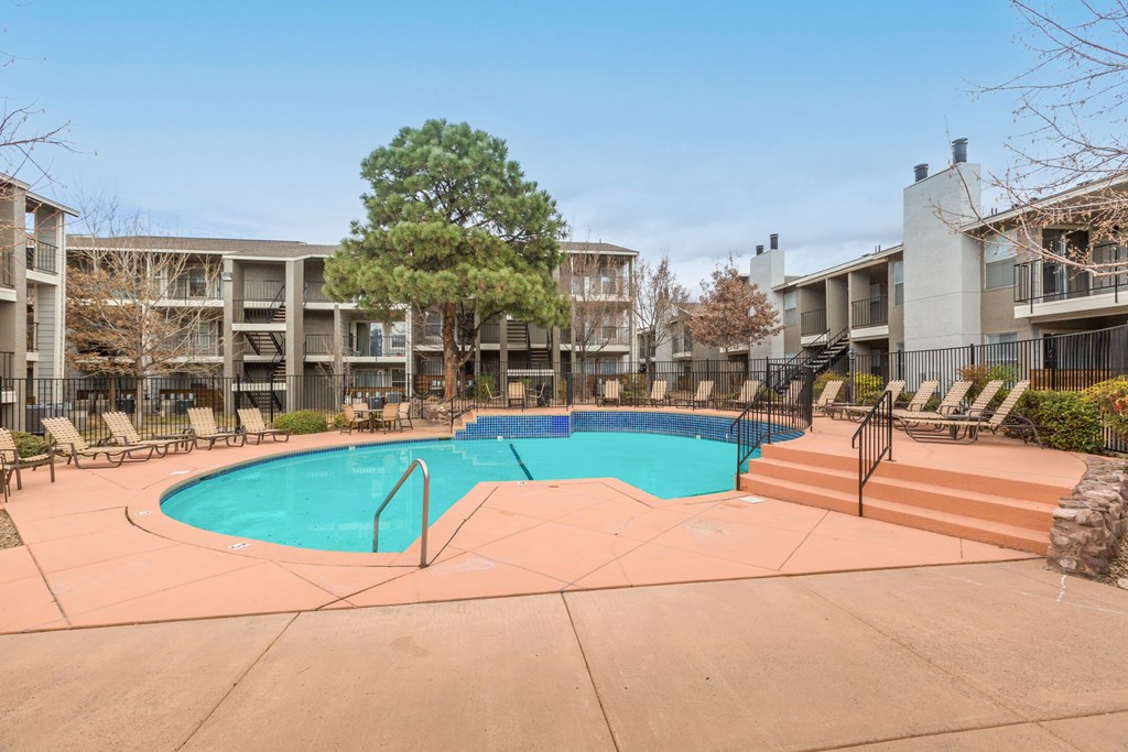 A swimming pool surrounded by lounge chairs and trees in a residential area.