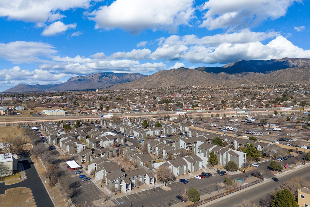A residential area with houses and cars under a blue sky with clouds.