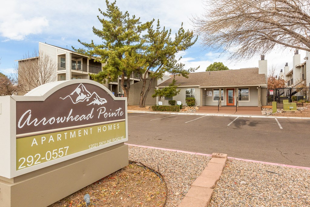 A brown and yellow sign for Arrowhead Pointe Apartment Homes sits in front of a parking lot.