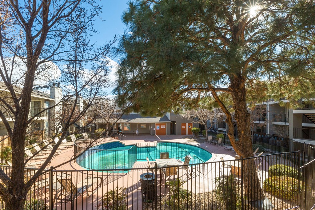 A pool surrounded by a fence with a tree in the foreground.