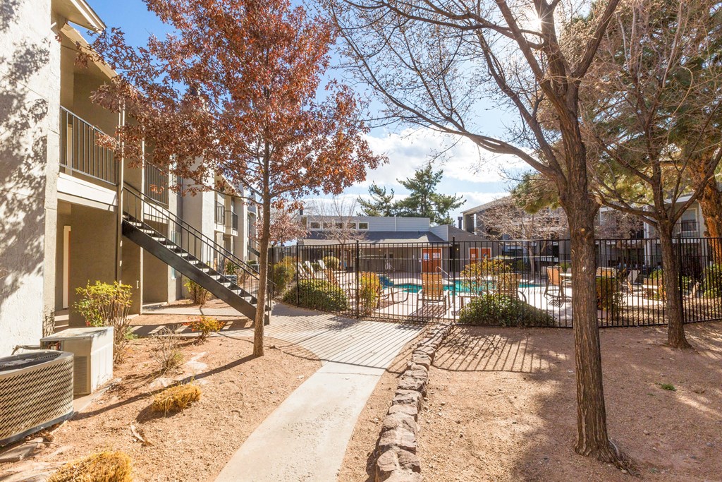 A courtyard with a fence, a tree, and a building in the background.