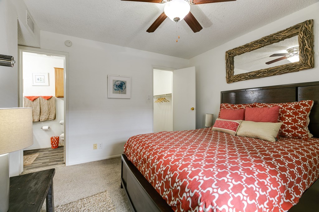 A bedroom with a patterned bedspread and a ceiling fan.