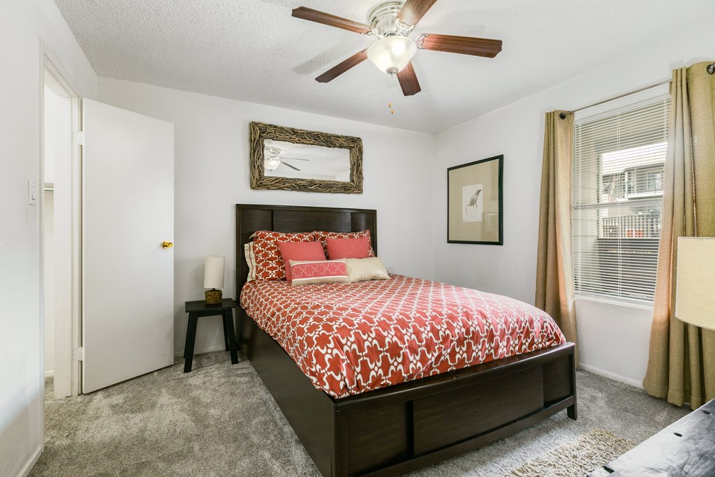 A bedroom with a bed, a ceiling fan, and a window with curtains.