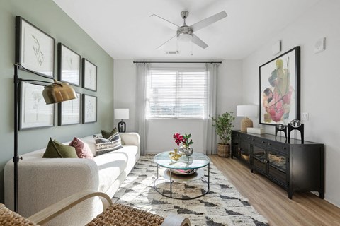 A living room with a white sofa, a glass coffee table, and a ceiling fan.