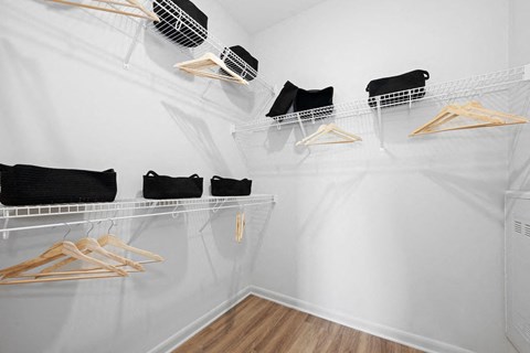 A white closet with clothes hanging on hangers.
