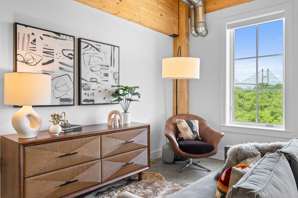 a living room with a large window and a dresser with a chair and lamp