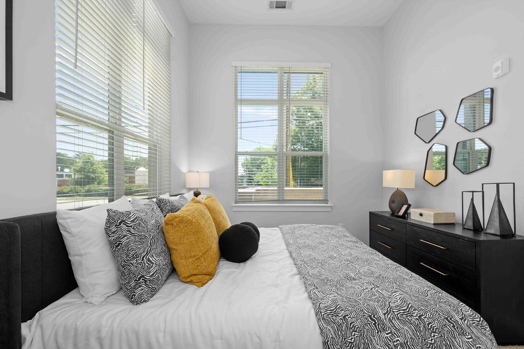 A bedroom with a large bed, a window with blinds, and a black dresser with a mirror.