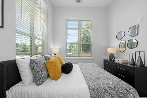 A bedroom with a large bed, a window with blinds, and a black dresser with a mirror.