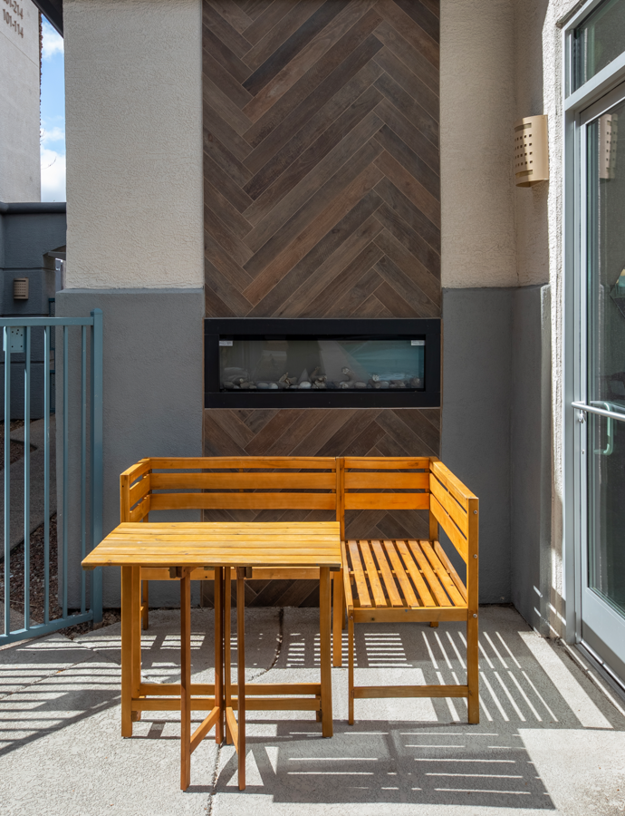a wooden table and bench sit on a balcony in front of a fireplace