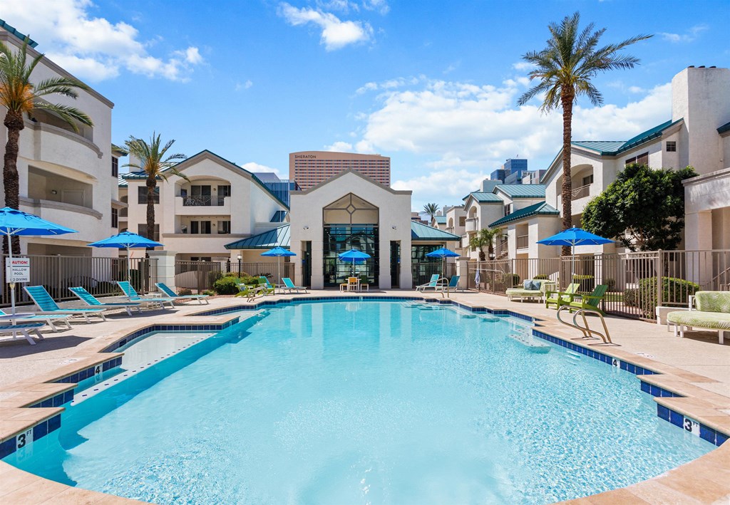 a large swimming pool with lounge chairs and umbrellas in front of a building