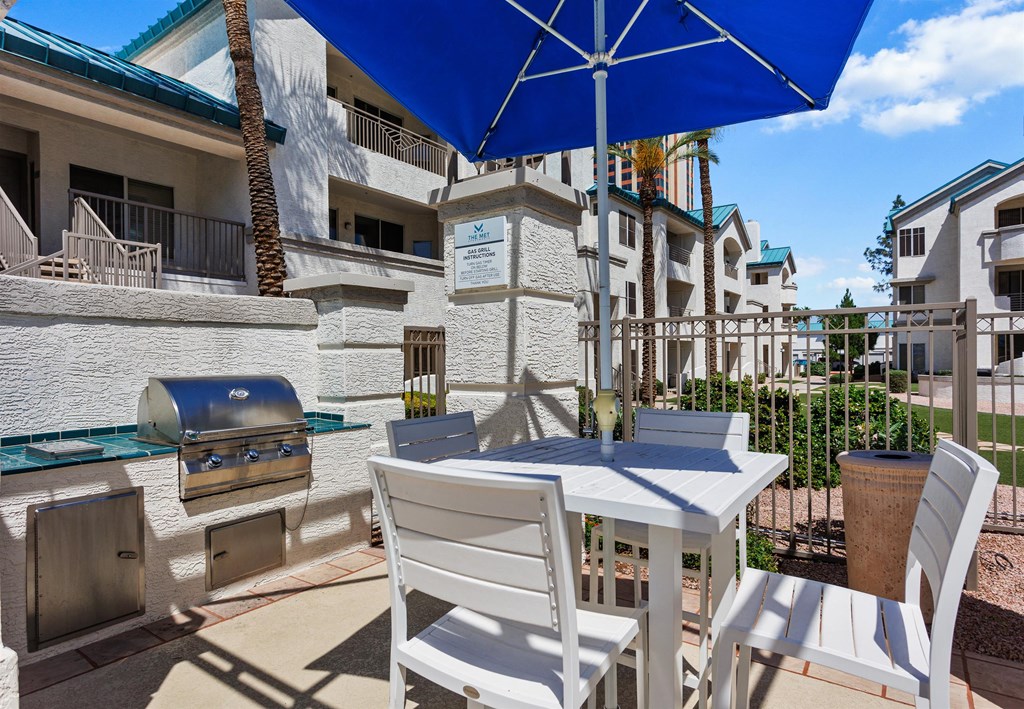 a table with two chairs and an umbrella on a patio with a grill and buildings in the