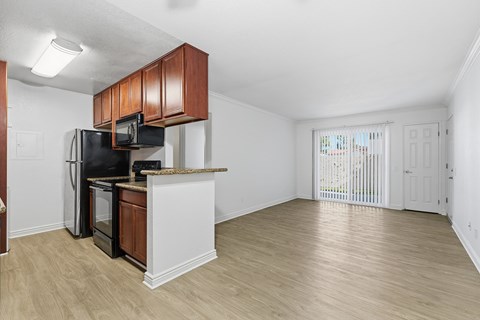 A kitchen with a black fridge and microwave, brown cabinets, and a white countertop.