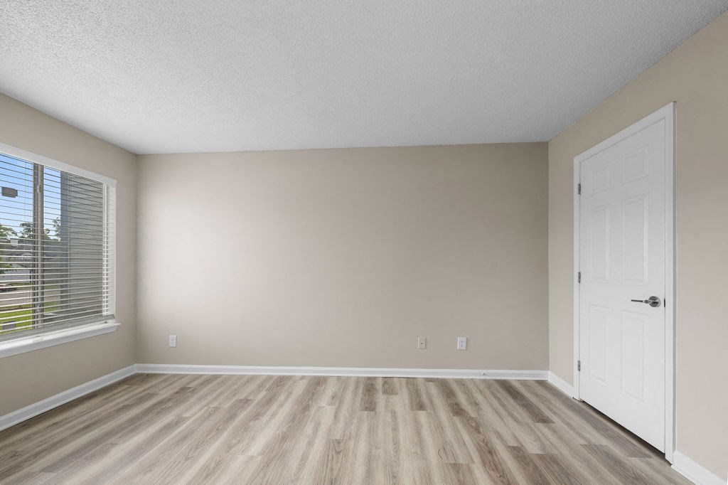 the spacious living room of an empty home with wood flooring and a window