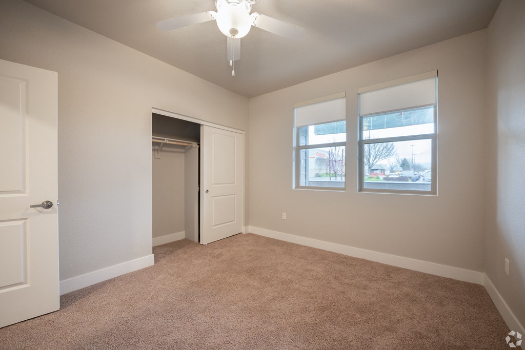 an empty living room with a ceiling fan and two windows