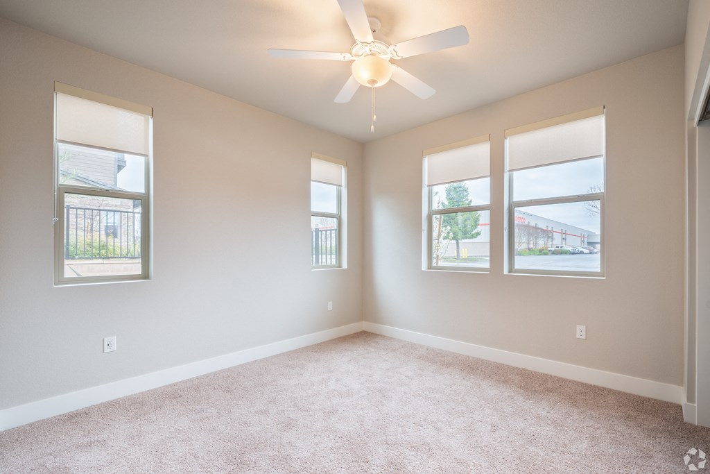 an empty living room with a ceiling fan and three windows