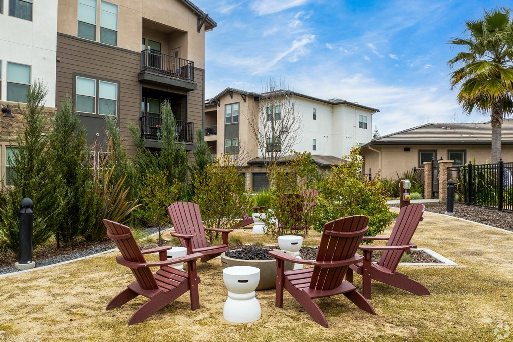 two red adirondack chairs sitting around a fire pit in front of apartments