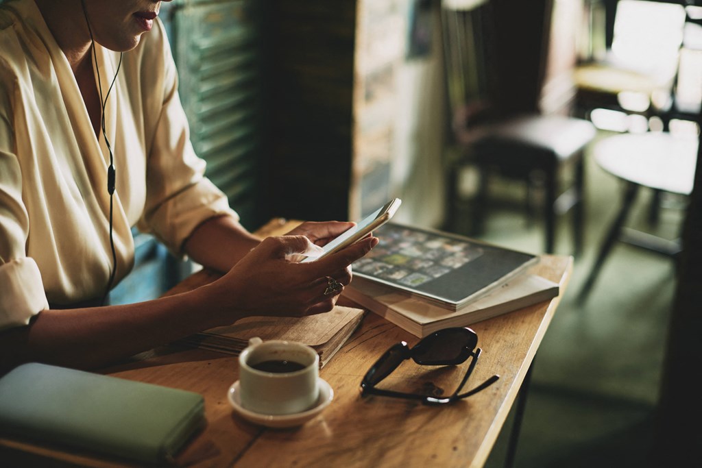 a woman sitting at a table using her cell phone and a laptop on a desk