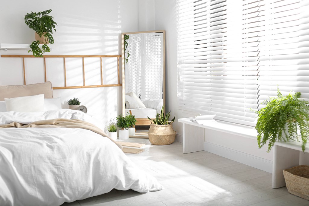 a white bedroom with a bed and a bathroom with a tub and plants