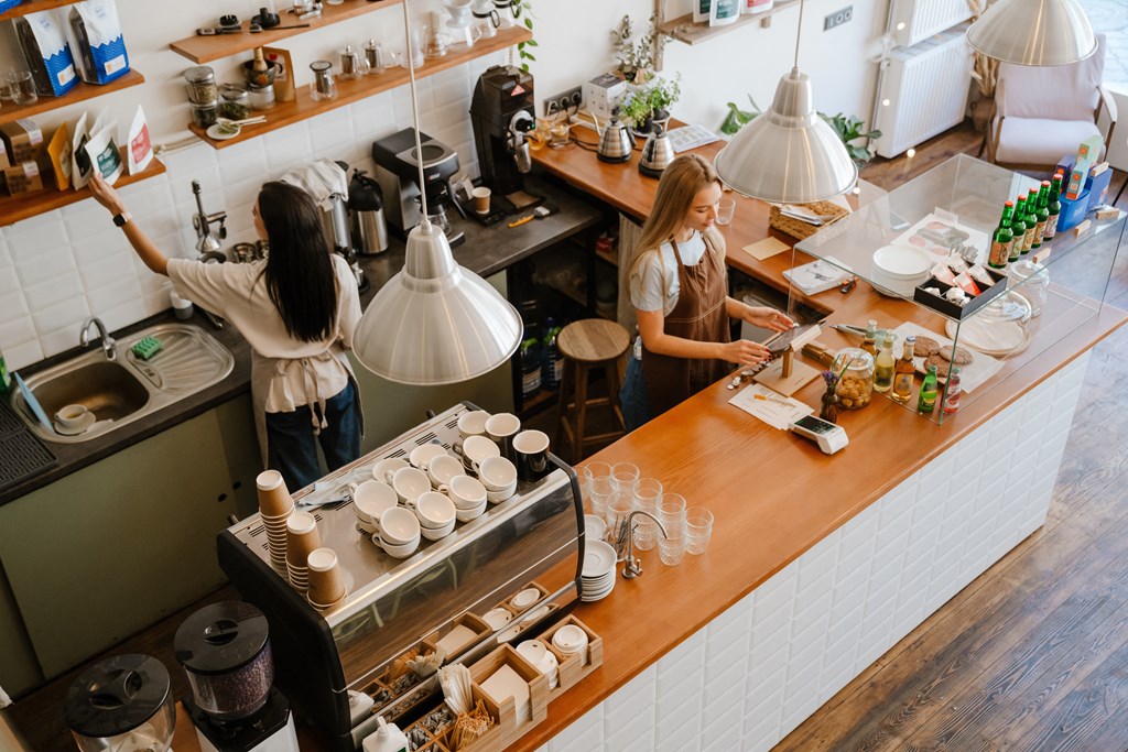 two women working in a coffee shop at the counter with a counter top espresso machine