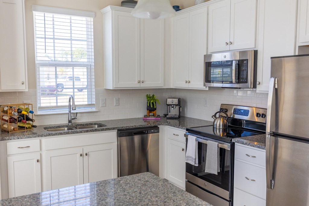 a kitchen with white cabinets and granite counter tops and stainless steel appliances