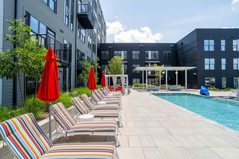 A pool area with red umbrellas and striped sun loungers.