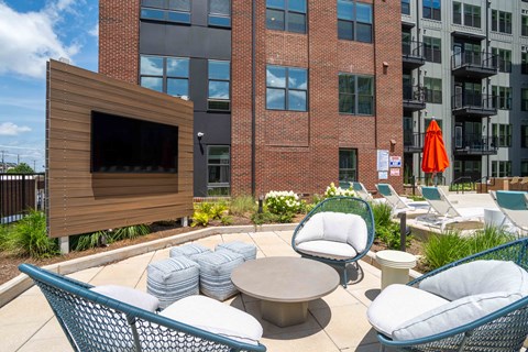 A modern outdoor seating area with a television and comfortable chairs.
