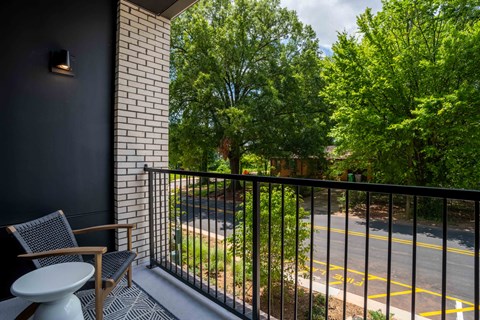 A balcony with a chair and table overlooking a street.
