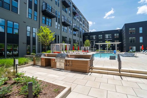 A sunny day at a modern apartment complex with a pool and sun loungers.