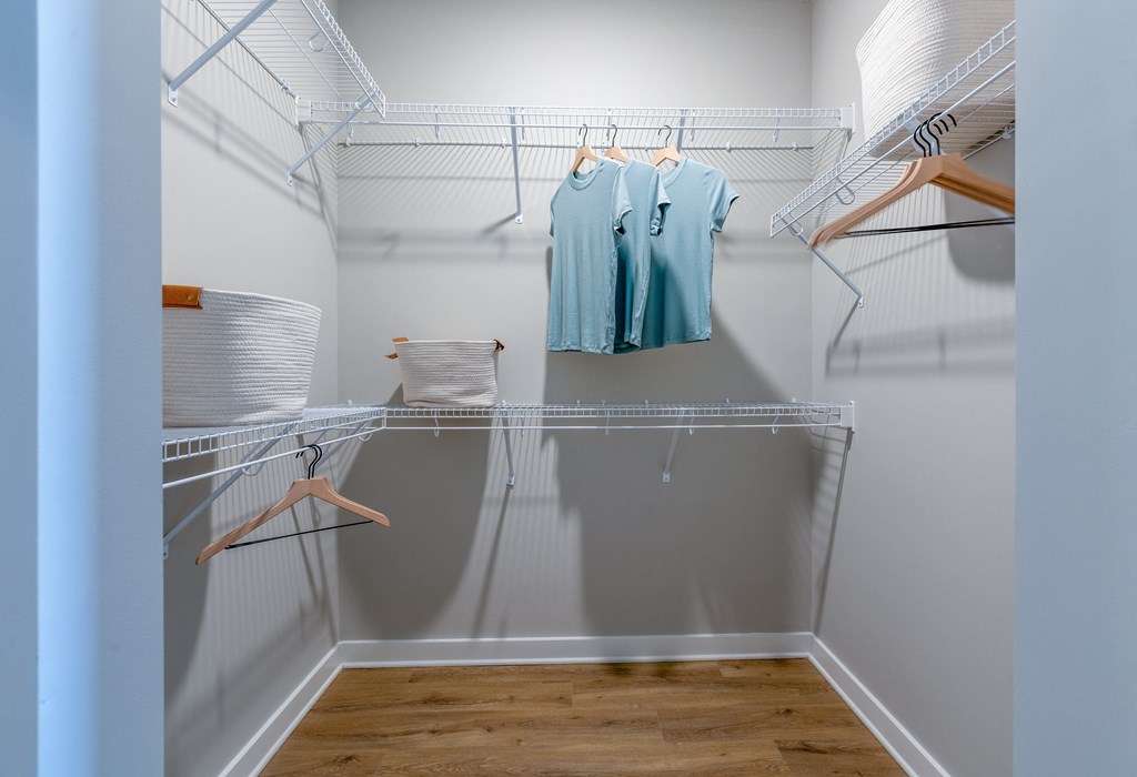 a spacious walk in closet with white walls and shelves and a hanging rack with clothes