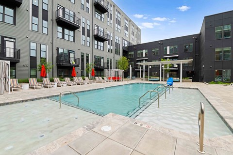 A swimming pool surrounded by chairs and umbrellas in front of a building.
