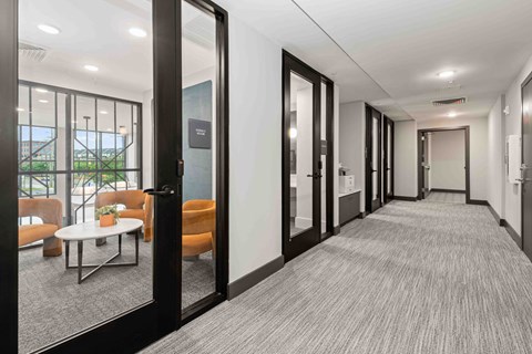 A hallway with a carpeted floor, a white table, and orange chairs.