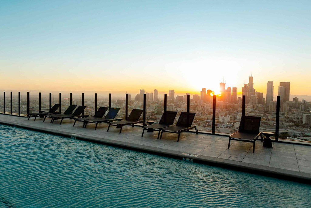 A poolside with chairs overlooking a city skyline at sunset.
