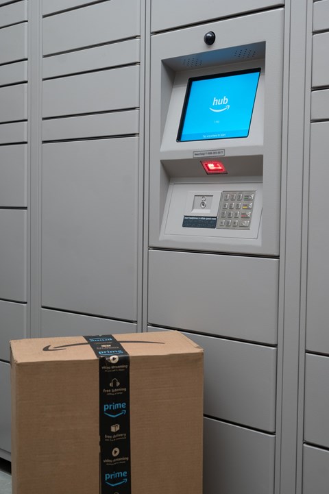 A cardboard box with a black prime sticker on it is in front of a grey locker with a blue screen on it.