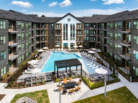 an outdoor pool with lounge chairs and tables in front of an apartment building