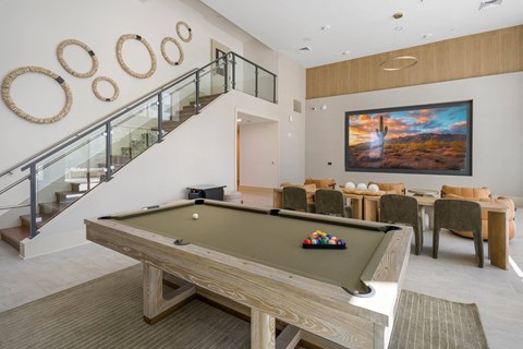 A pool table is in the middle of a room with a staircase and a painting on the wall.