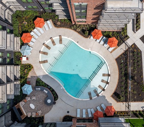 An aerial view of a swimming pool surrounded by orange umbrellas and concrete structures.
