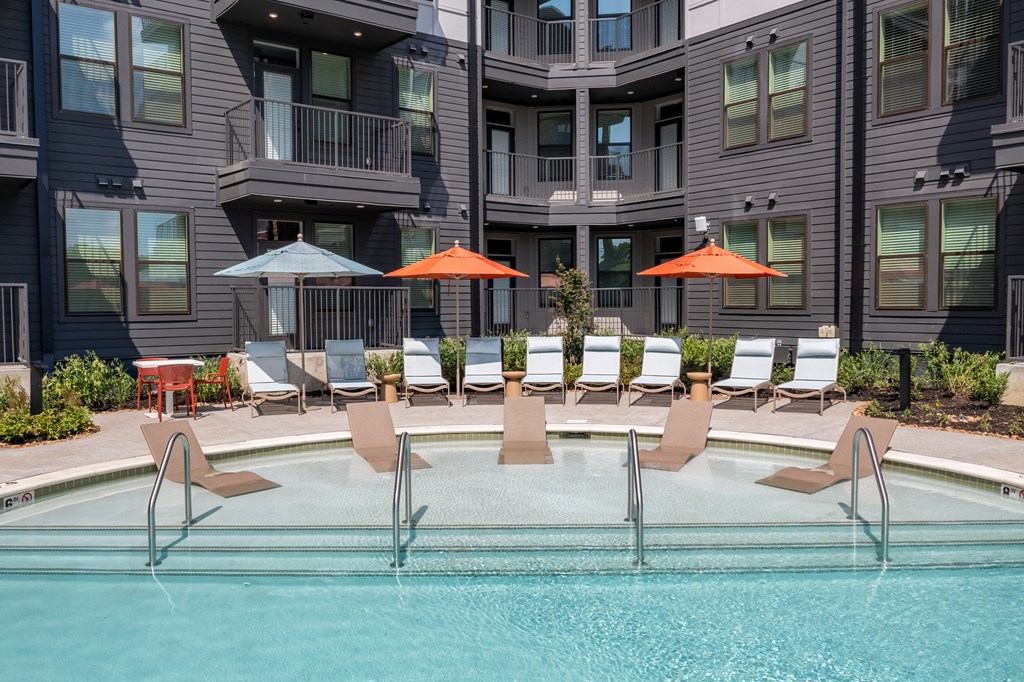 A pool with chairs and umbrellas in front of a building.