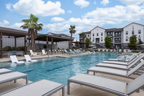 A pool with sun loungers and a building in the background.
