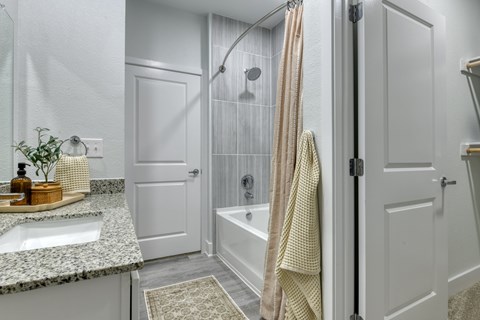 A bathroom with a sink, a shower, and a towel hanging on the door.