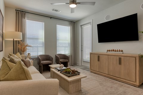 A living room with a beige sofa, a wooden coffee table, a flat screen TV, and a ceiling fan.