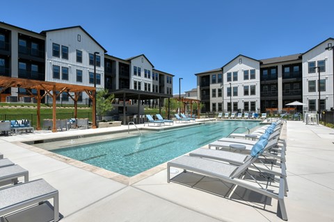 A large swimming pool with sun loungers and a building in the background.